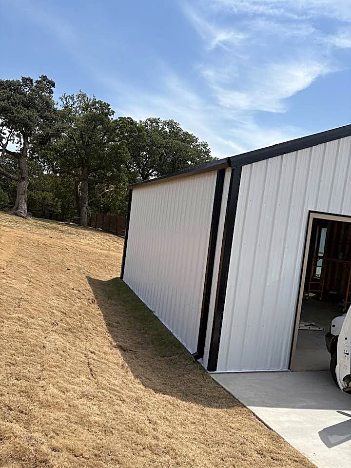 A white metal building with dark trim standing on a graded lot.