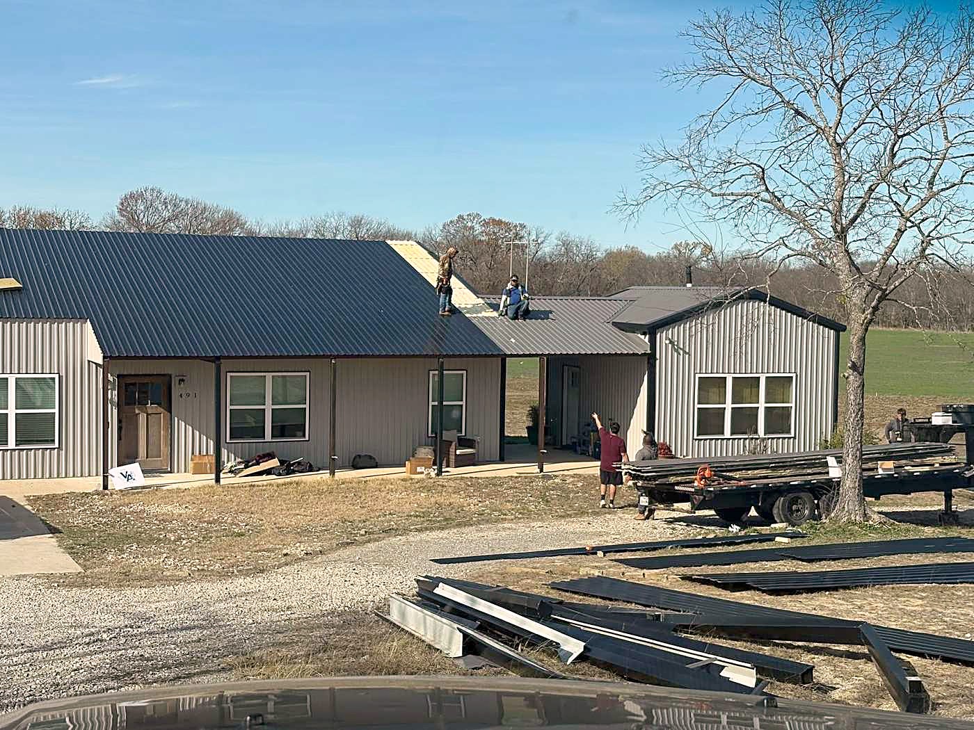 A metal clad house with a new dark metal roof going on and panels stacked in the drive.