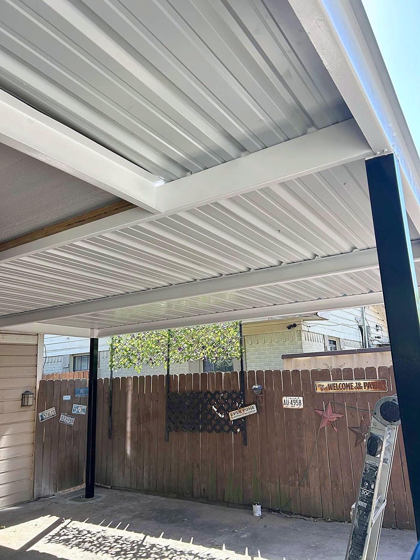 The white underside of a metal carport roof over a concrete drive.