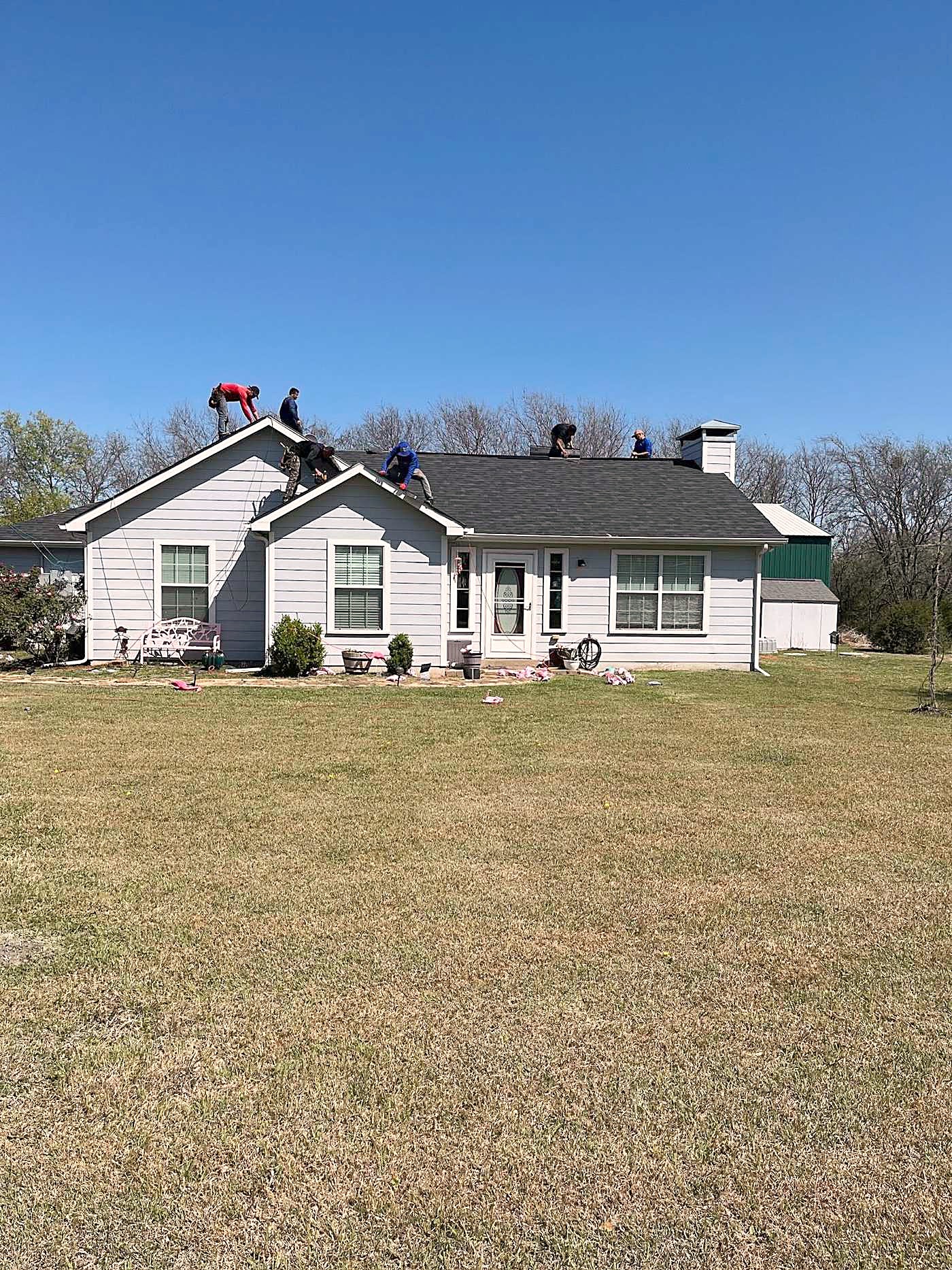 A white farmhouse with a crew working across the roof on a clear day.