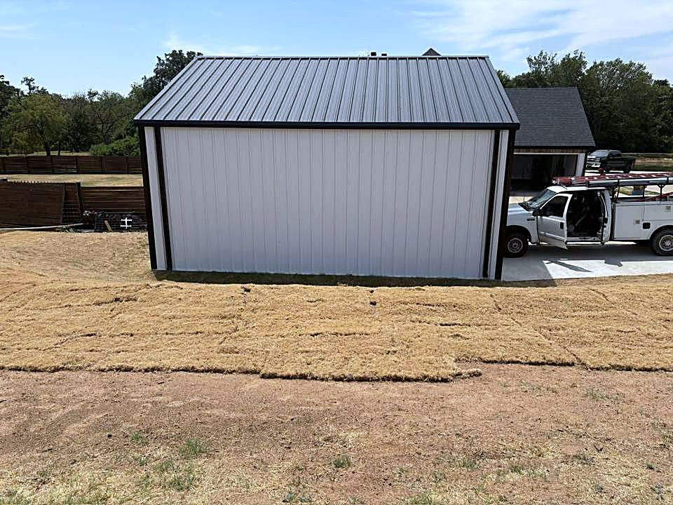 A grey metal garage building with a dark metal roof and a work truck parked beside it.
