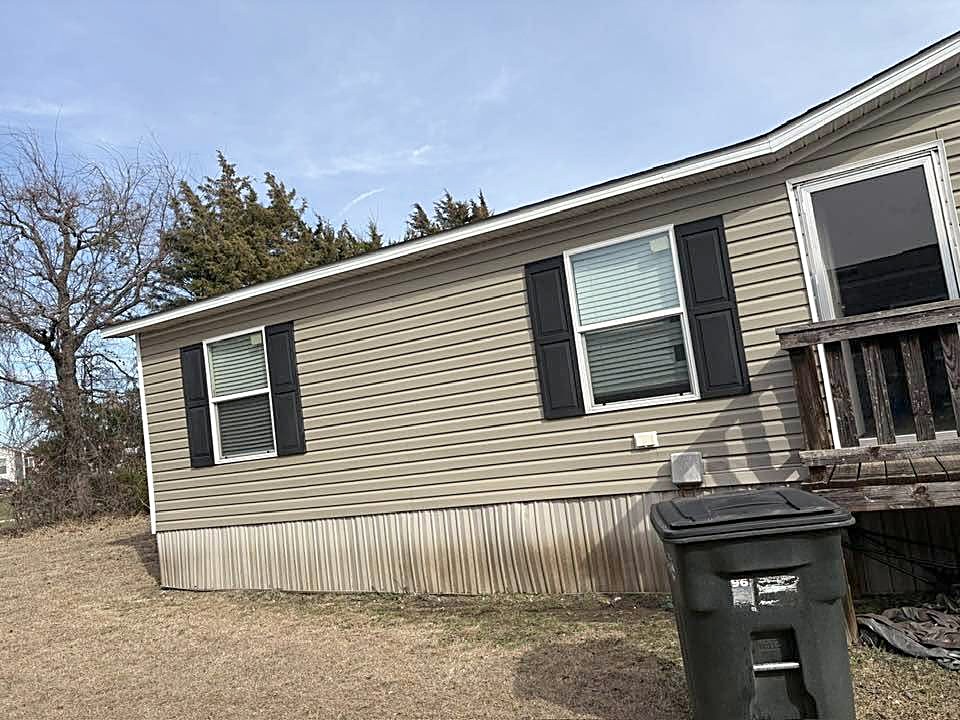 A manufactured home with new tan siding and black shutters.